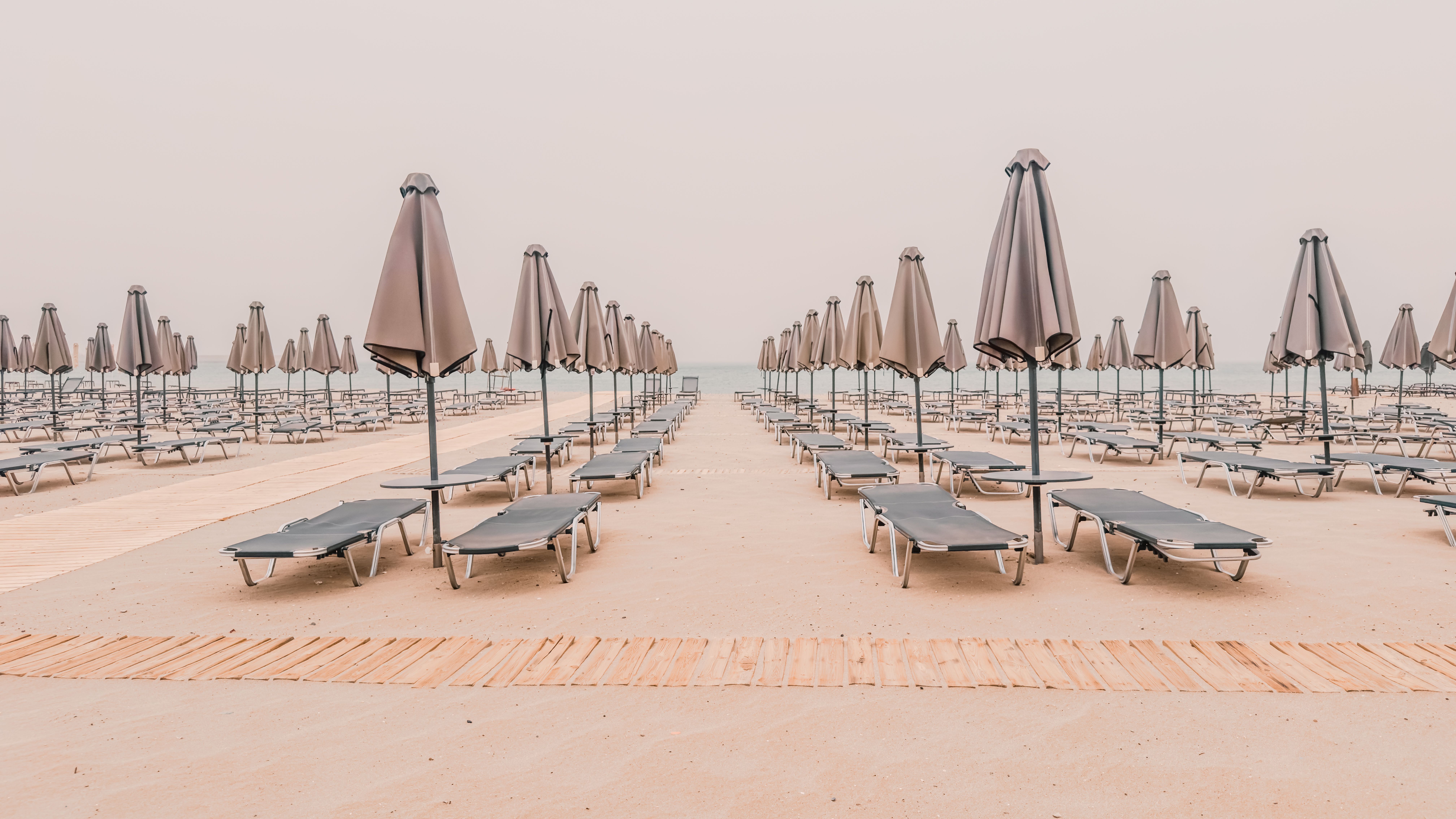 Uma praia deserta com cadeiras e guarda-sóis alinhados, transmitindo sensação de tranquilidade e lazer ao ar livre.