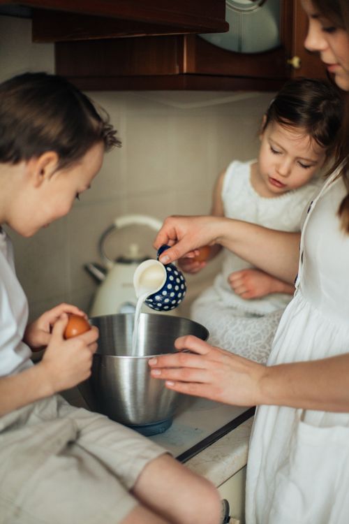 Free Mother and children baking in a kitchen, pouring milk into a bowl. Stock Photo