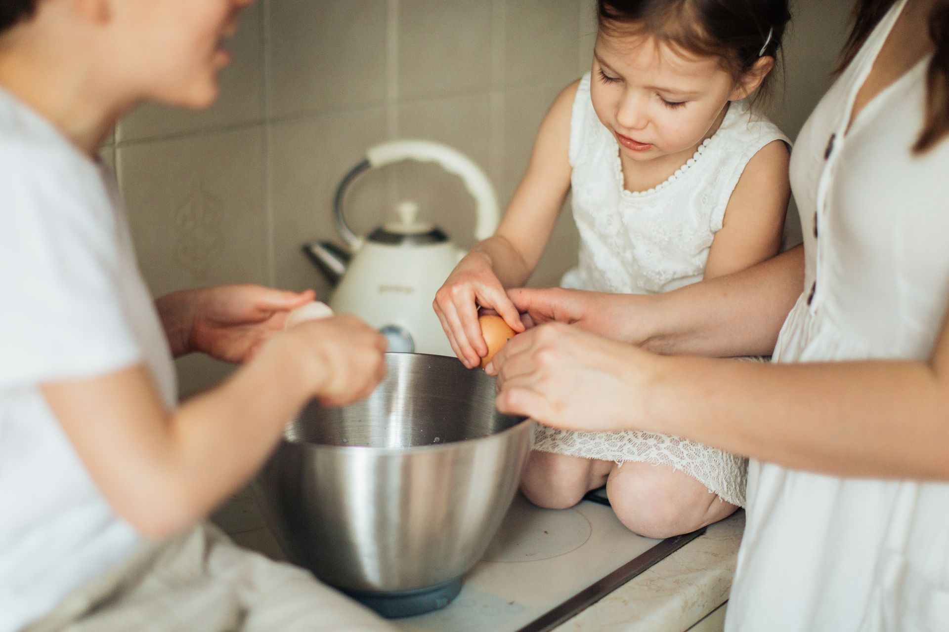 Children and adult in kitchen cracking eggs into a bowl, enjoying a family baking activity.