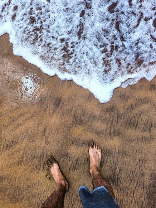 Free Feet in sand with waves approaching the shore, capturing a serene beach moment. Stock Photo