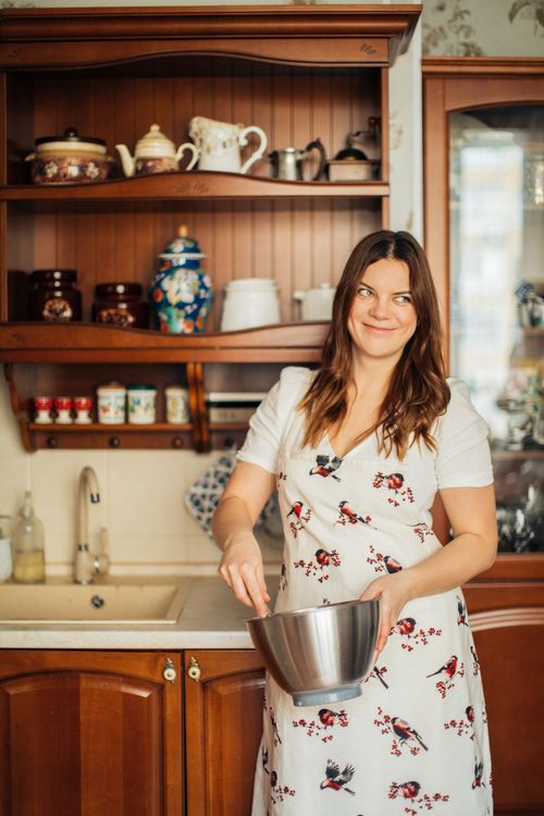 Free Smiling woman in a floral dress mixing ingredients in a cozy kitchen setting. Stock Photo