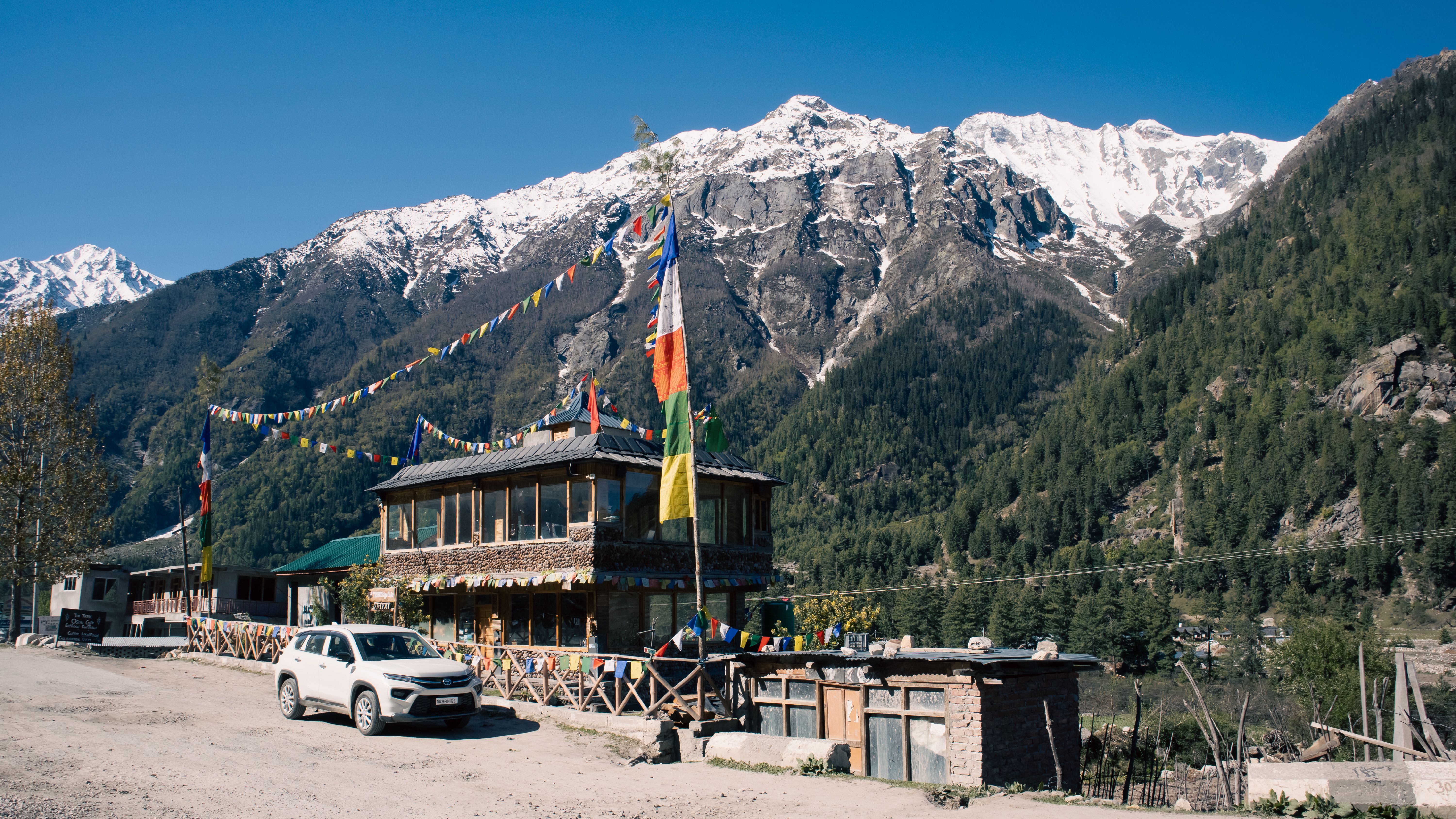 Scenic view of a mountain lodge with prayer flags under snow-capped peaks.