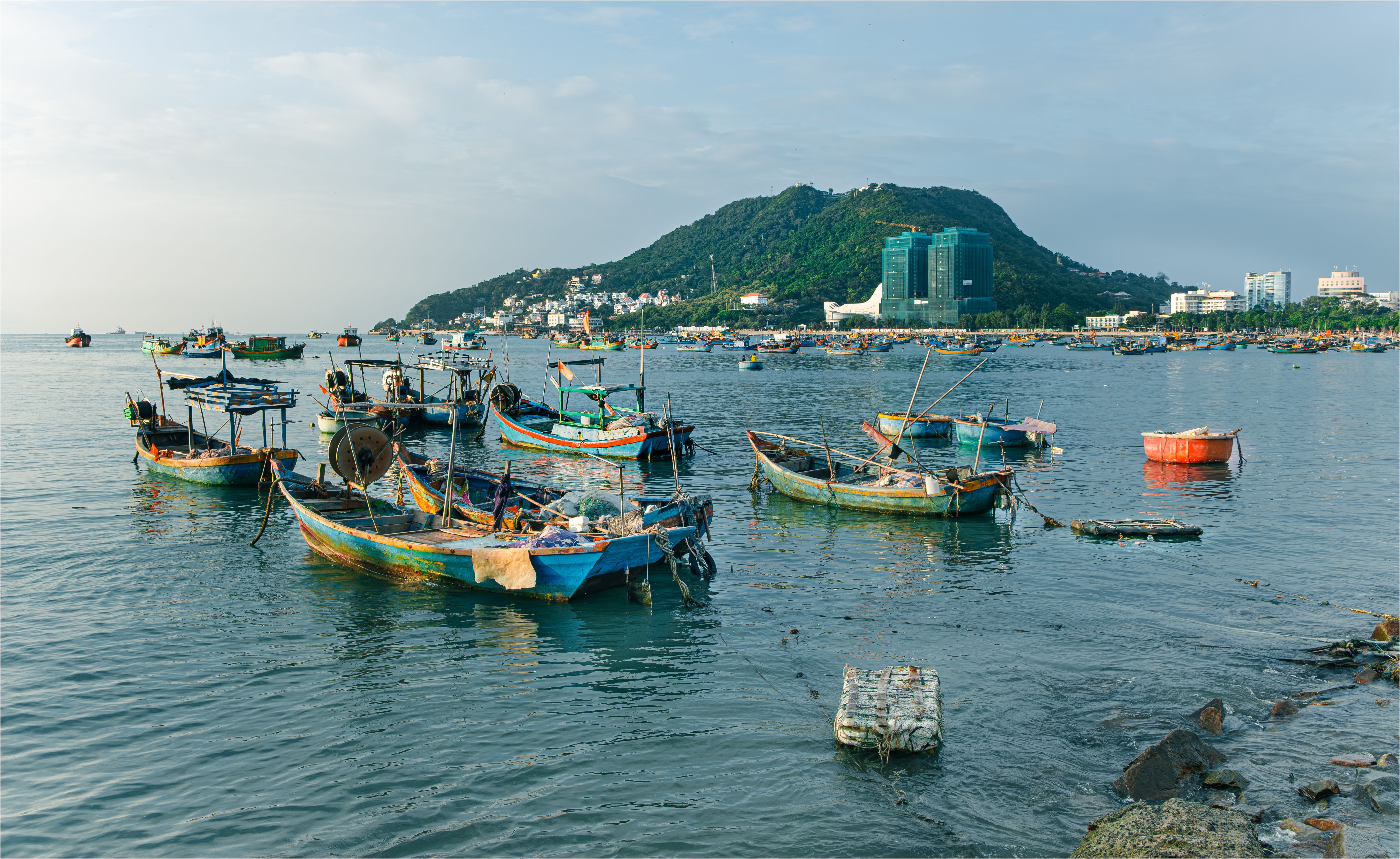 Scenic view of traditional fishing boats on the sea in Ho Chi Minh City, Vietnam with a lush green hill background.