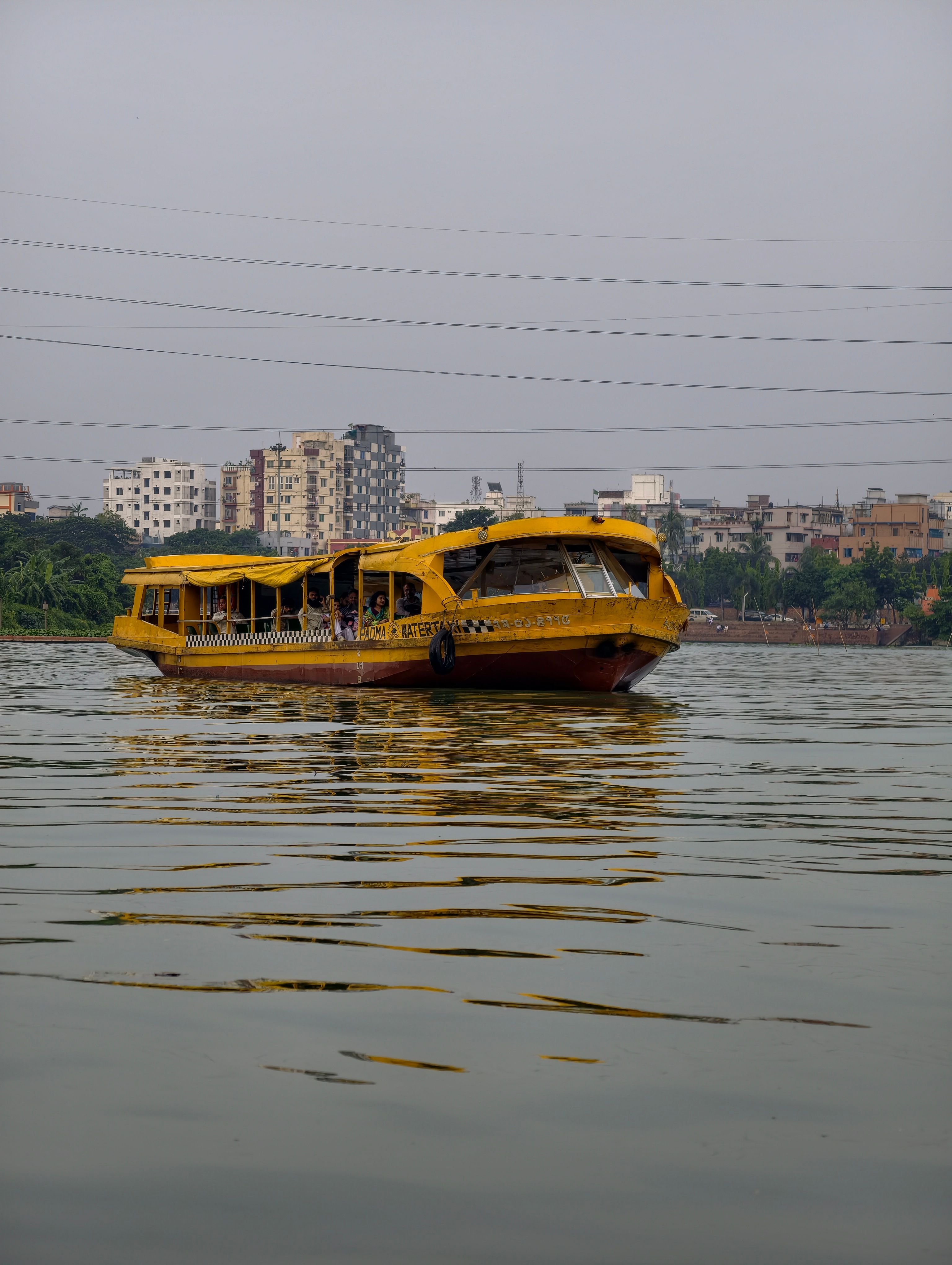 A vibrant yellow passenger boat navigates a calm urban river with city skyline in the background.