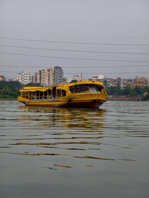 Free A vibrant yellow passenger boat navigates a calm urban river with city skyline in the background. Stock Photo