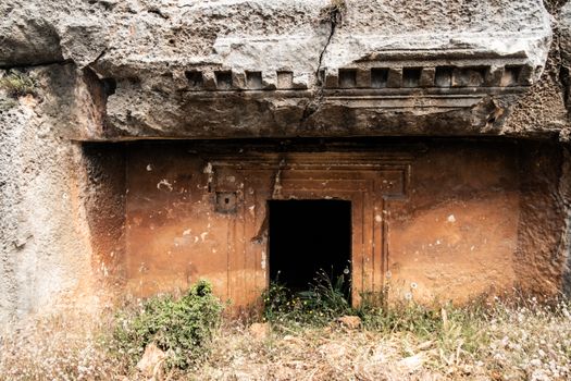 Explore the mysterious entrance of an ancient rock-cut tomb amidst ruins.
