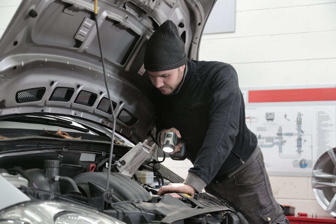 Free Man in Black Jacket and Black Knit Cap Inspecting Car Engine Stock Photo