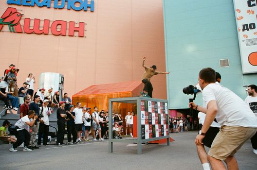 Skateboarder performs trick at outdoor festival in Moscow, Russia. Crowd watches closely.