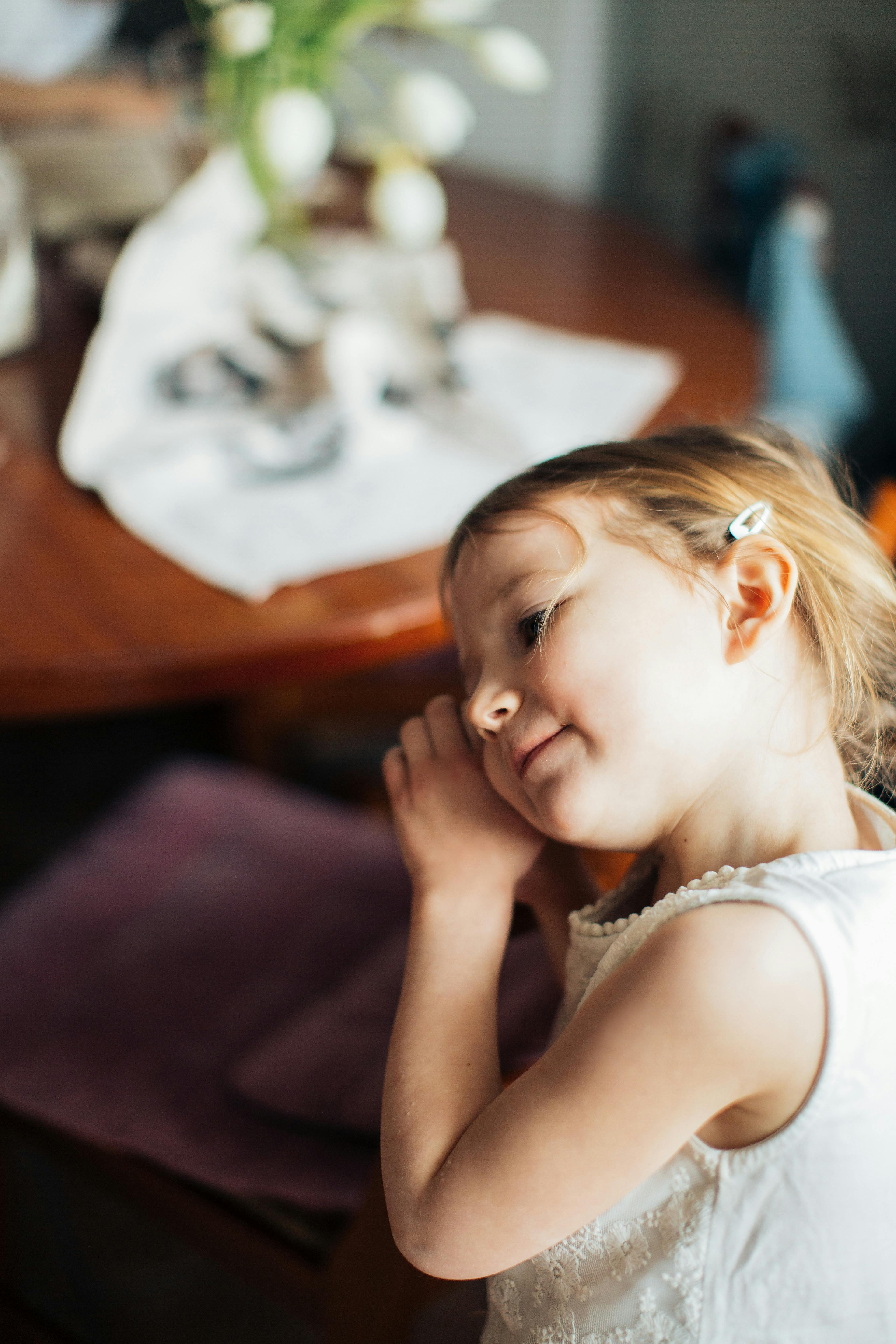 一位身着白色连衣裙的年轻女孩在室内带着柔和的微笑做着白日梦，尽显天真与魅力