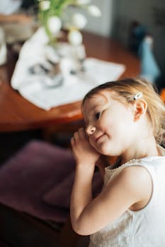 一位身着白色连衣裙的年轻女孩在室内带着柔和的微笑做着白日梦，尽显天真与魅力