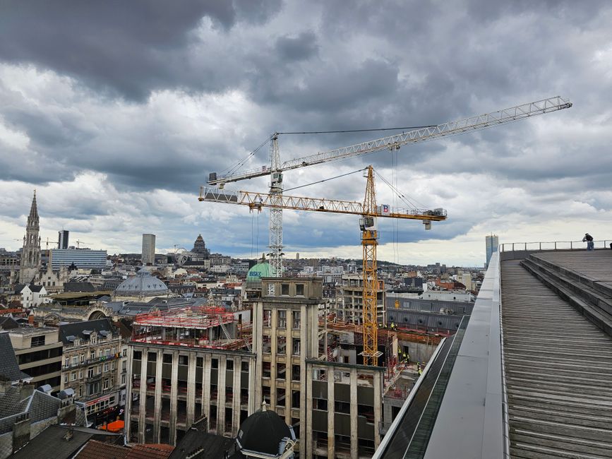 View of cranes over a cityscape with dramatic cloudy skies, indicating urban development.