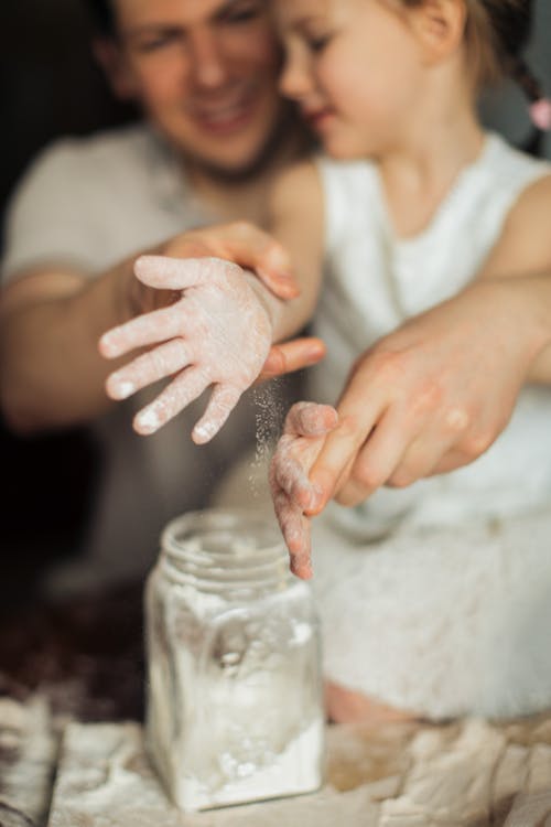 Free Happy crop cute girl with pigtail and blurred father shaking off flour from hands while making dough Stock Photo