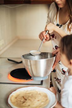 Woman and girl making pancakes on an electric stove in a cozy kitchen setting.