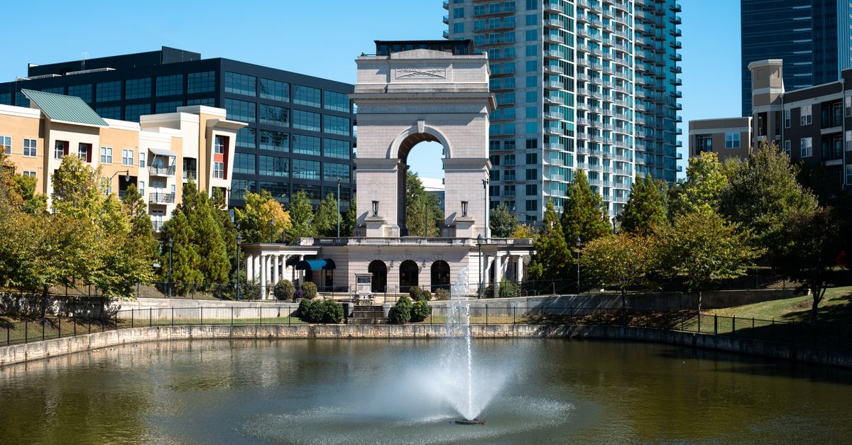 A scenic view of the Millennium Gate with reflections in a fountain, surrounded by Atlanta's cityscape.