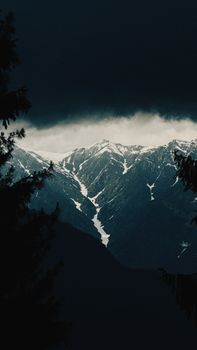 Dramatic view of snow-capped mountains under stormy clouds in Naggar, Himachal Pradesh.