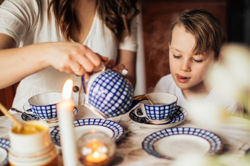 Free Child drinking tea with a stylish checkered blue teapot and saucer set. Warm and cozy indoor scene. Stock Photo