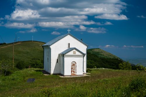 Free Picturesque view of a white chapel situated amidst lush Georgian hills under a vibrant blue sky. Stock Photo