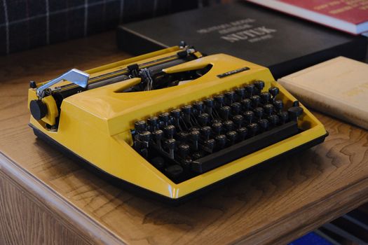 A retro yellow typewriter on a wooden desk with books, capturing a nostalgic vibe.