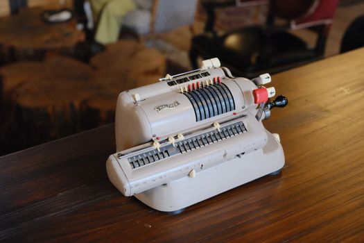 A vintage mechanical calculator resting on a rustic wooden table in a cozy indoor setting.