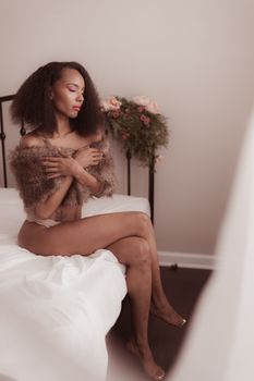 Serene woman sitting on bed in soft lighting, embracing tranquility.