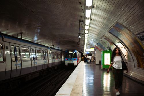 Free A woman walks in a dimly lit Paris metro station next to a parked train, capturing urban life. Stock Photo
