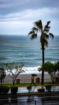 A lone person with umbrella walking along Alanya's coast on a rainy day.