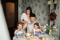 Contented family drinking tea with crepes together while sitting at table with candles at cozy kitchen with cuckoo clock on wall