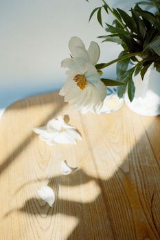 Sunlit white flowers on a wooden table create a serene and artistic atmosphere.