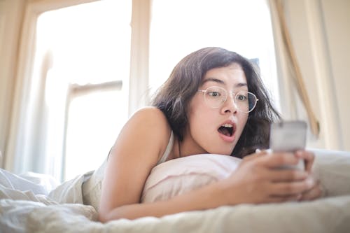 Free Woman Lying on Bed Holding Smartphone Stock Photo
