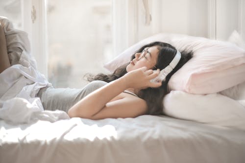 Free Woman Lying on Bed While Listening to Music Stock Photo