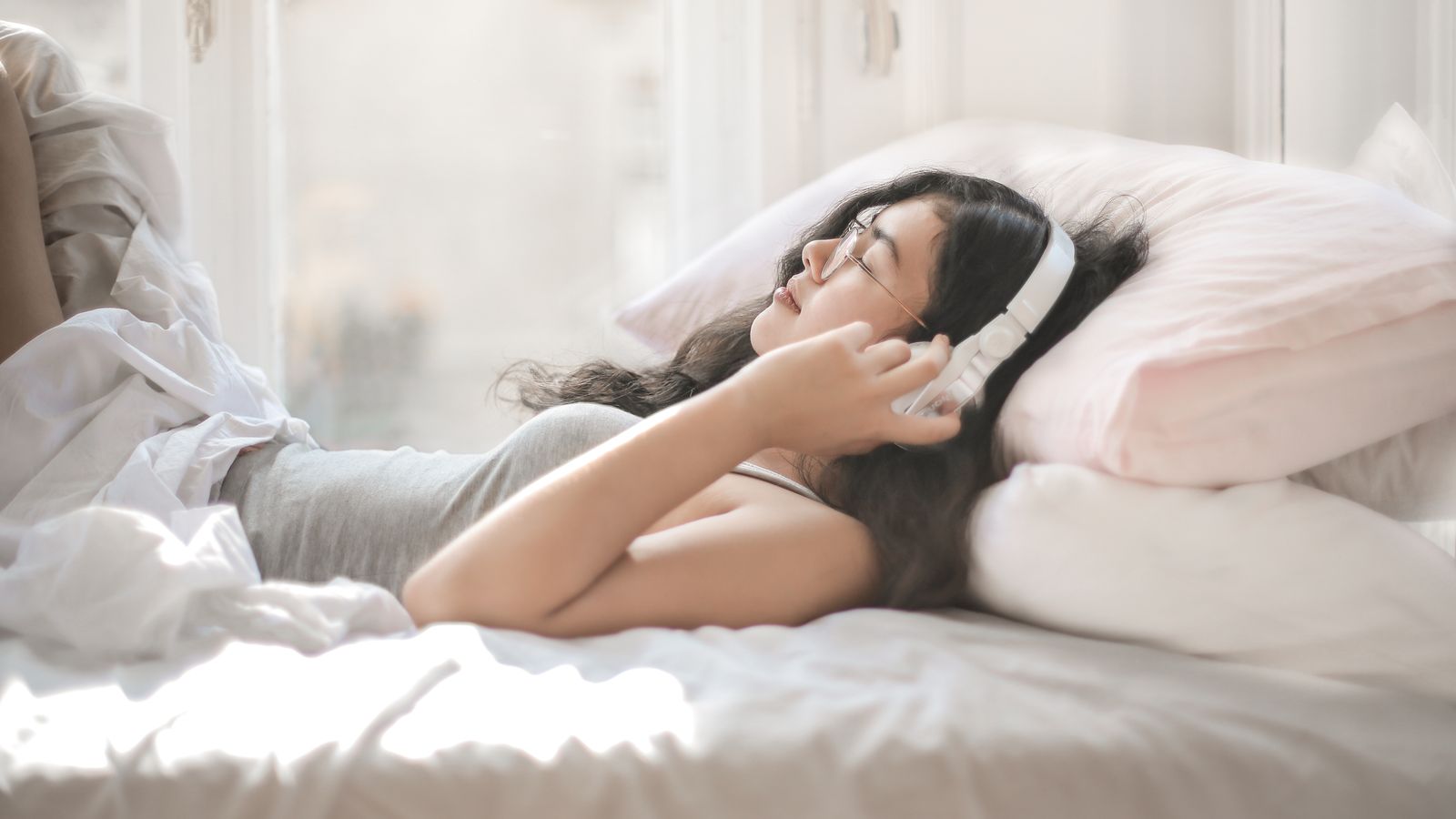 A woman lying on a bed listening through over-ear headphones