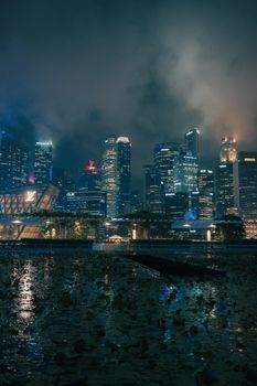 Dramatic nighttime view of Singapore's illuminated skyline with city lights reflecting on water.