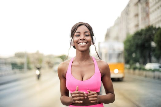 Joyful young woman in a pink sports bra running in an urban street, smiling and listening to music.
