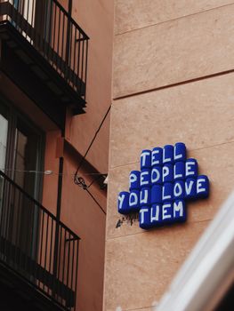 Inspirational street art in Barcelona with the message 'Tell People You Love Them' in blue letters.