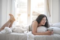 一位微笑的女人在舒适的卧室里，正用智能手机享受放松和舒适
