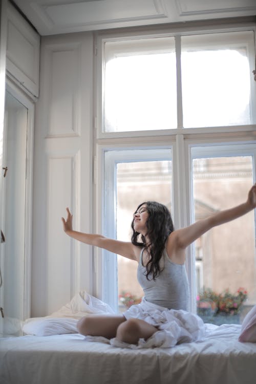 Free Photo of Woman in Gray Tank Top While Sitting on Bed Stock Photo