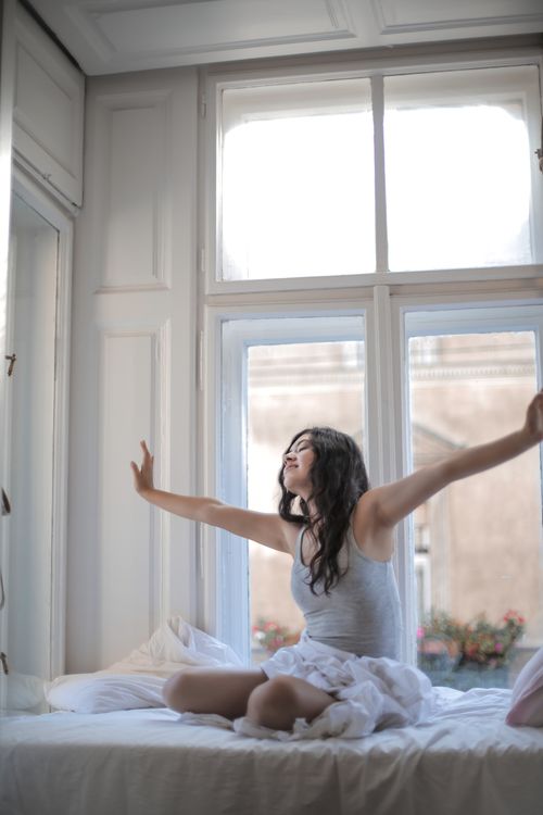 Free A woman enjoys the morning sunlight as she stretches in bed, feeling relaxed and refreshed. Stock Photo