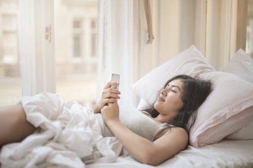 Free Young woman using smartphone in bed Stock Photo