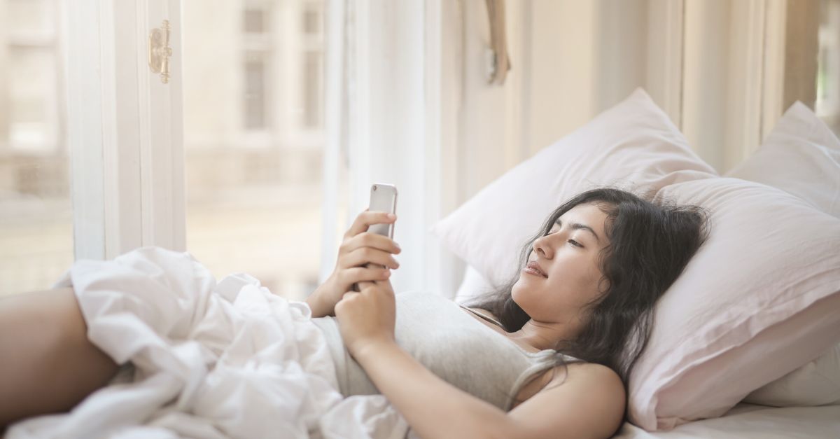 Young woman lying in bed looking at her phone in the morning light