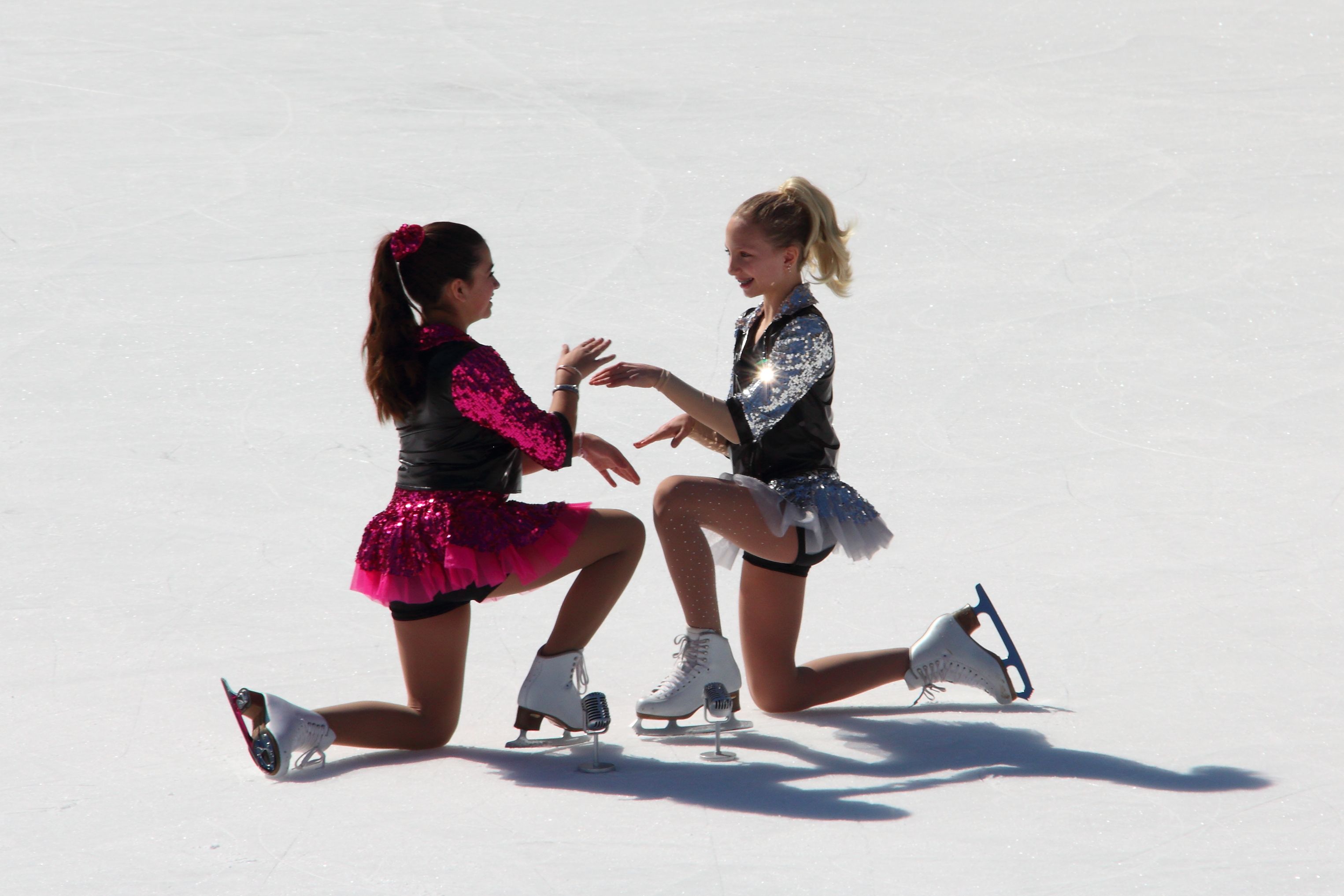 Two female ice skaters in colorful outfits enjoying a joyful moment on the ice.