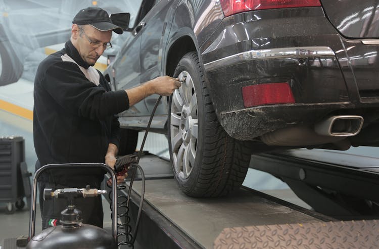 Serious Car Mechanic Pumping Up Car Wheel In Modern Service Garage