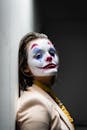 一名女子画着怪异的小丑妆，倚靠墙壁，创作出一幅黑暗而富有戏剧性的肖像