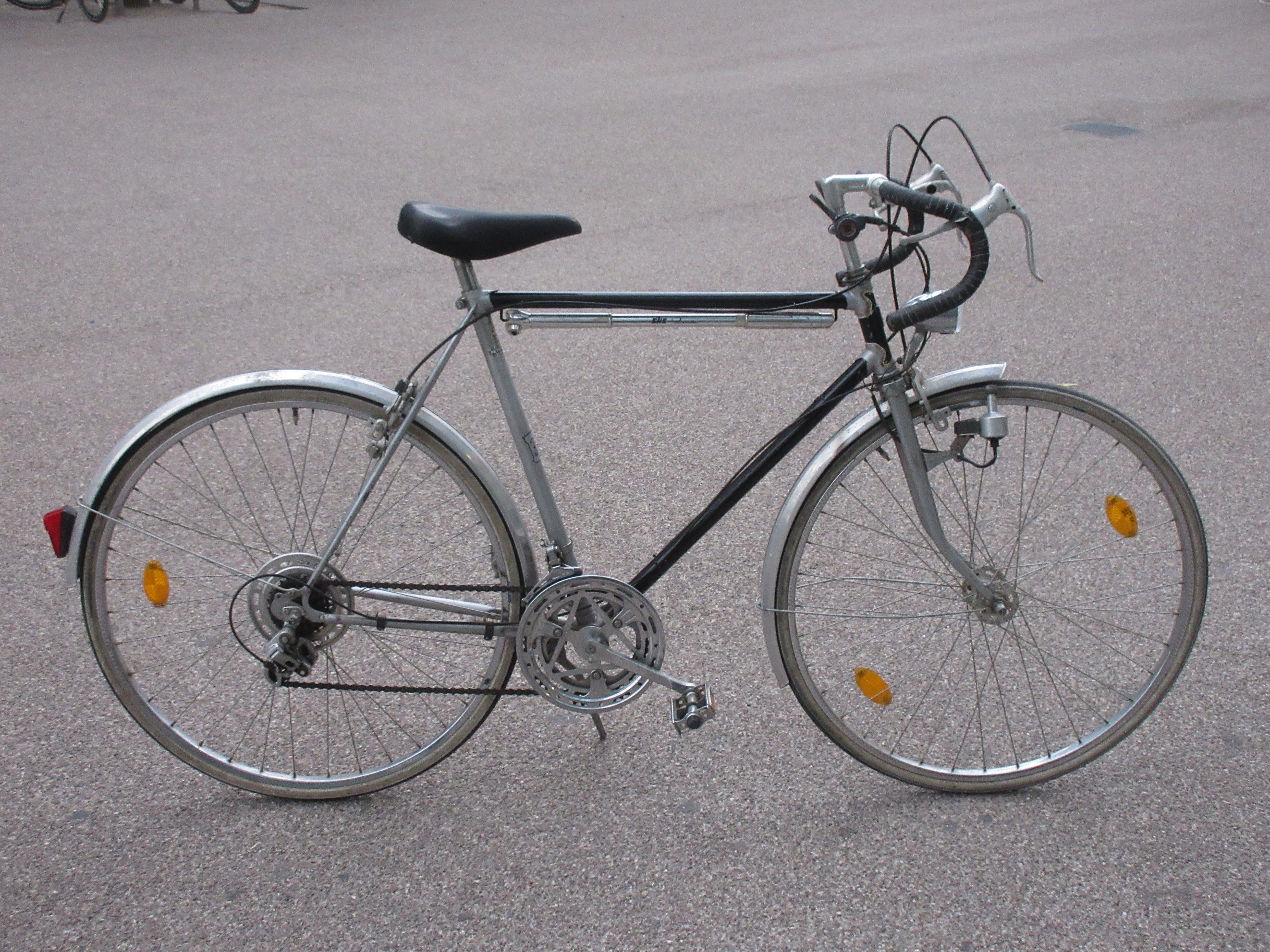 A classic silver vintage bicycle with drop handlebars photographed outdoors on pavement.