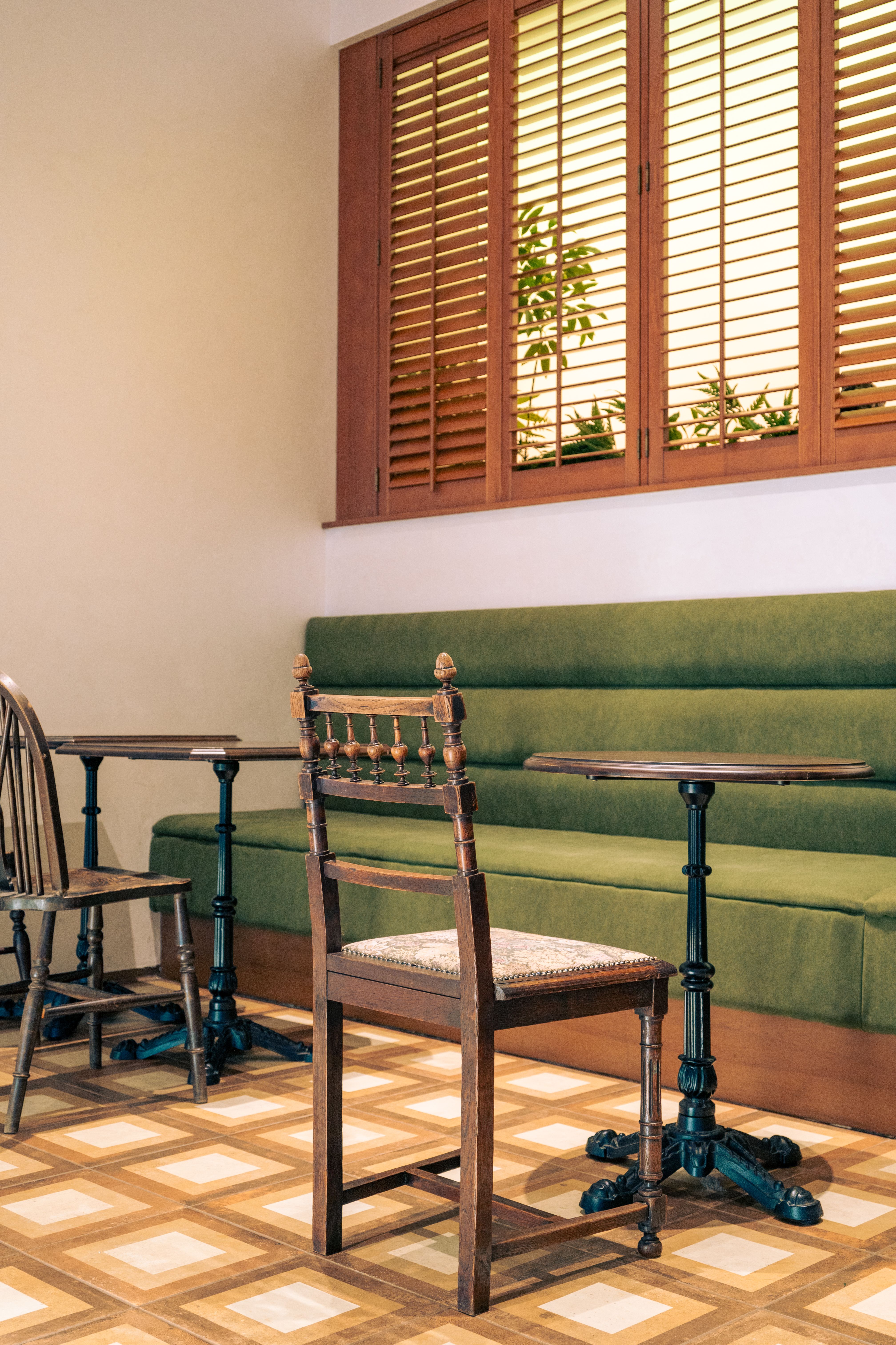 Salle de café : banquette verte, guéridons en bois et chaise ancienne