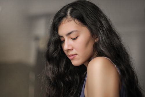 Free A serene portrait of a young woman with long dark hair, eyes closed, in a soft light. Stock Photo