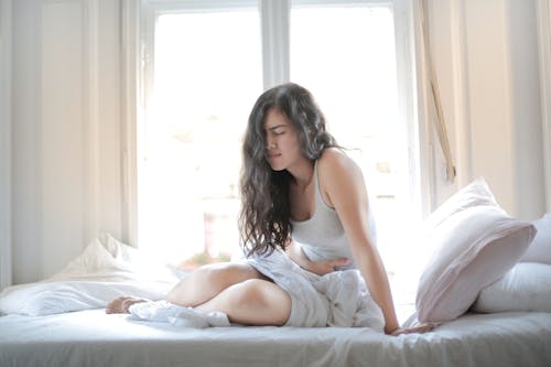 Woman in Gray Tank Top While Sitting on Bed