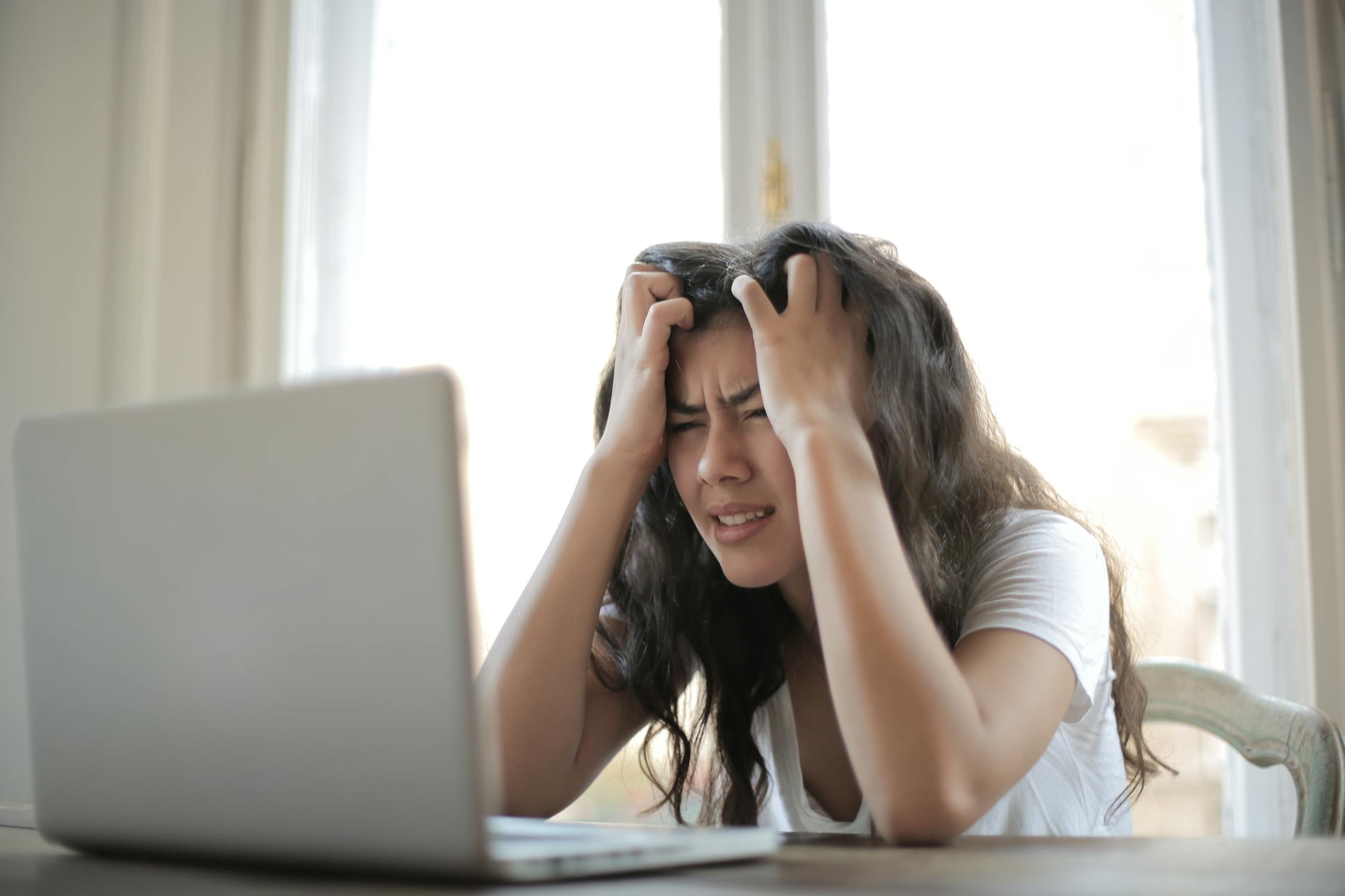 Woman in white top looking frustrated at laptop, unable to find content writing that answers her question. 