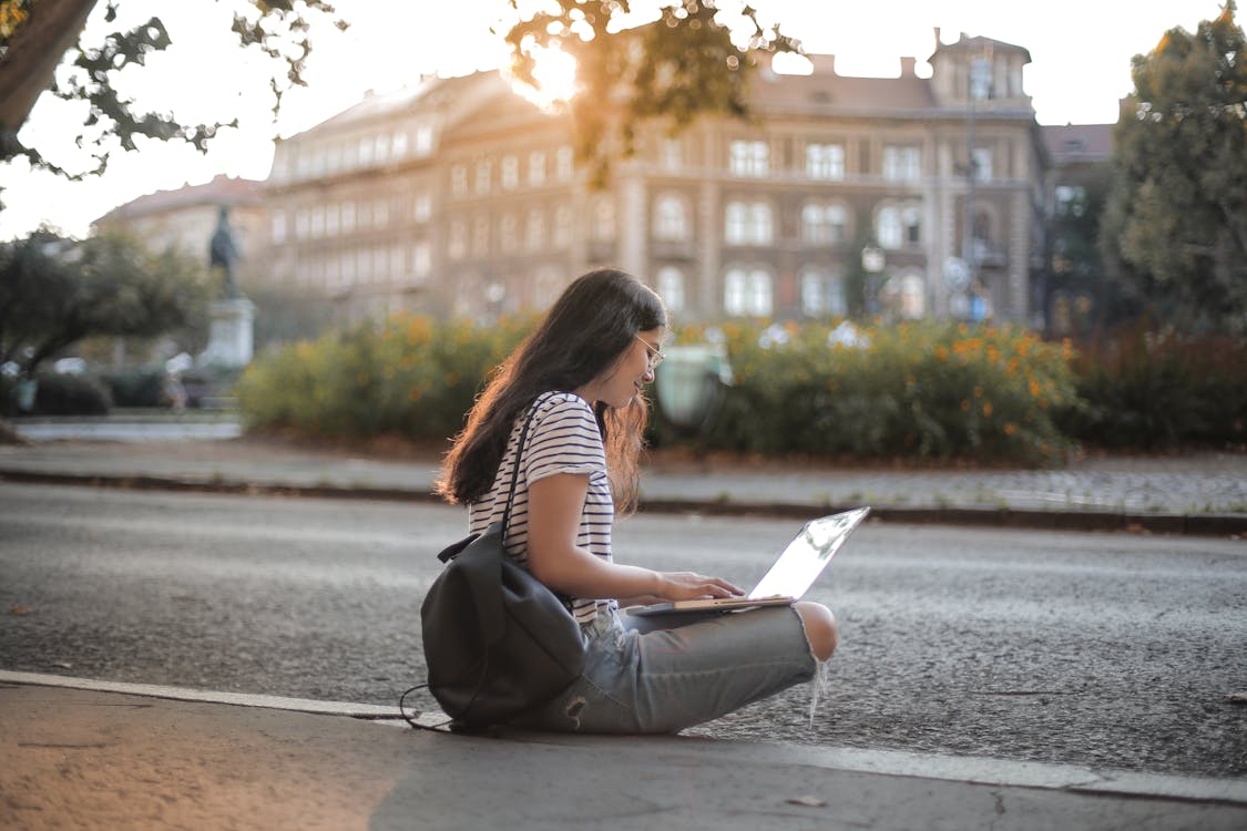 Woman in Black and White Stripe Shirt and Blue Denim Jeans Sitting on Sidewalk