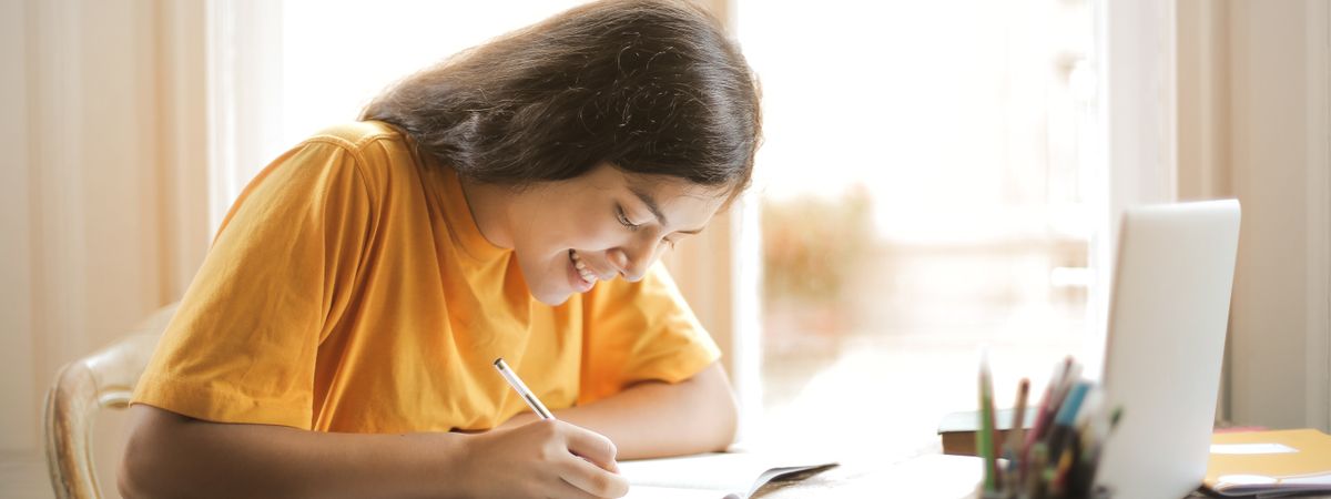 Estudiante tomando apuntes junto a un portátil