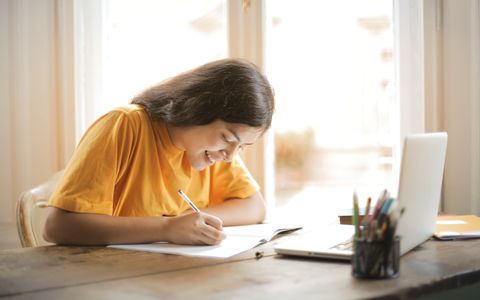 Estudiante tomando apuntes junto a un portátil